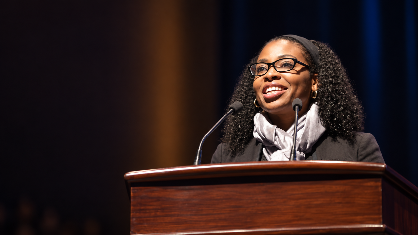 Dr. Nadine Richards speaking at a podium in an institutional setting